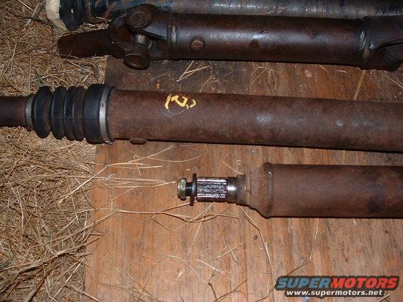 Several rusty driveshafts laid out on a wooden surface with straw. One has a black rubber boot