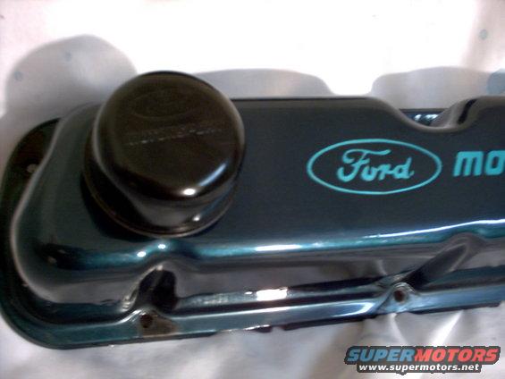 Dark teal Ford valve cover with blue oval Ford logo and 'motor' text. Black oil cap on top
