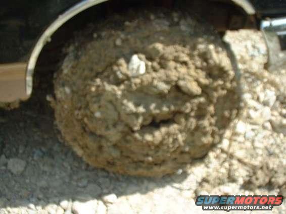 Mud-caked tire on a vehicle, likely stuck in dirt