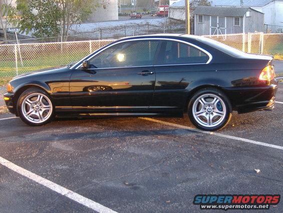 Black coupe parked in a lot. It has silver rims and blue brake calipers