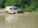 1989 GMC Jimmy - An SUV navigates a water crossing, its tires submerged in the muddy water.