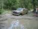 1989 GMC Jimmy - A tan SUV is stuck in a muddy, wooded area, with a person standing nearby.