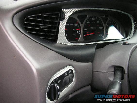 Dashboard interior of a 1999 Ford Taurus, showing the instrument cluster, air vent, and headlight controls with carbon fiber trim