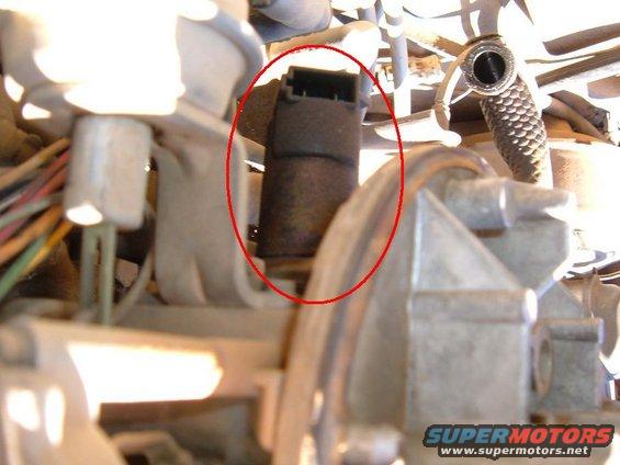 Close-up of a dark, cylindrical engine part with a black electrical connector on top, circled in red