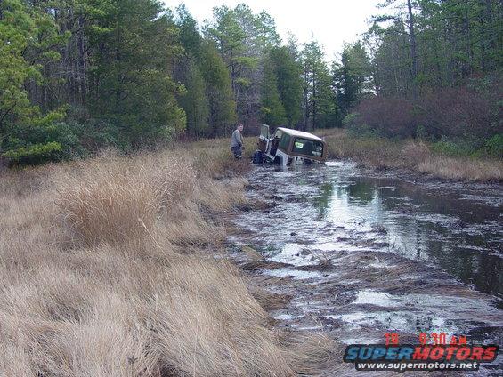 Jeep partially submerged in muddy water with a person standing nearby