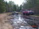 1995 Dodge 1500 - Two off-road vehicles are stuck in a muddy, watery ditch surrounded by trees.
