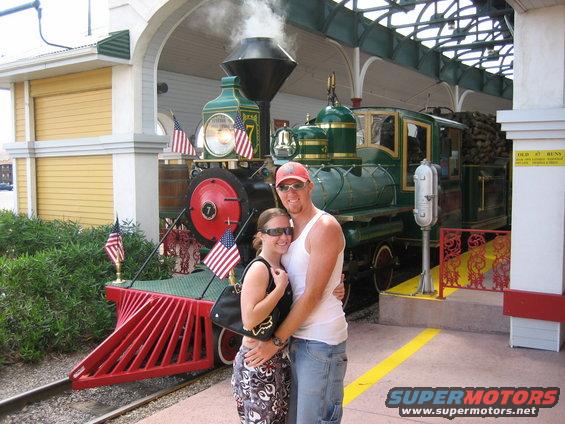 Couple posing in front of a green steam locomotive with American flags