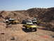 1996 Ford Bronco - Several off-road vehicles navigate a dusty desert terrain under a clear blue sky.