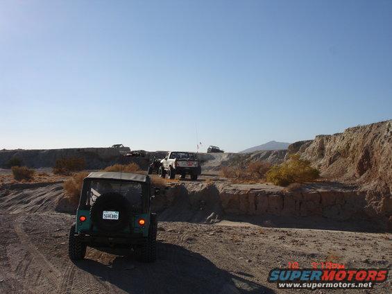 Green Jeep Wrangler rear view on dirt road with other off-road vehicles in background