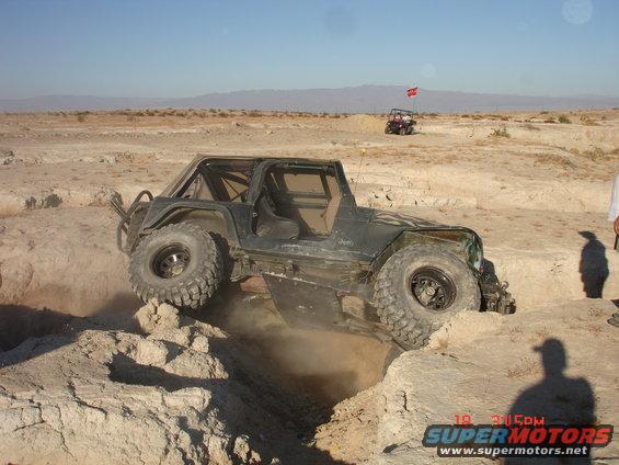 Dark green Jeep Wrangler off-roading over dirt mounds, front right wheel elevated