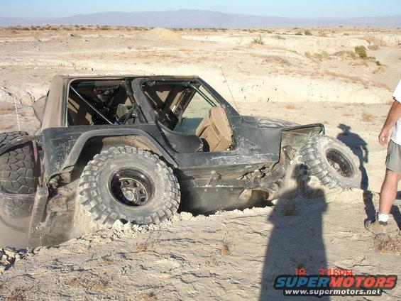 Dark green Jeep Wrangler stuck in dirt with large tires, driver's side visible