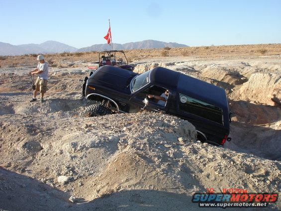 Black SUV tilted in a dirt ditch with a person standing nearby and another vehicle behind it