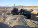 1996 Ford Bronco - A black SUV is stuck in a deep ditch off-road, with a person attempting to help and another vehicle in the background.