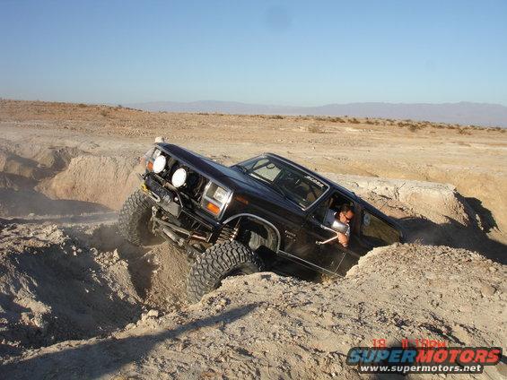 Black 1996 Ford Bronco with large tires navigating a dirt trench, driver visible
