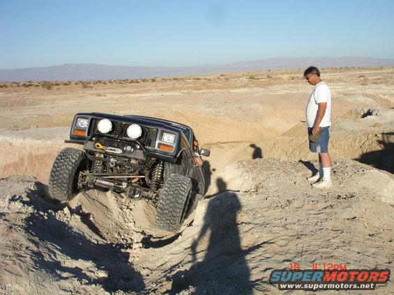 Black off-road SUV climbing a dirt hill with large tires and auxiliary lights