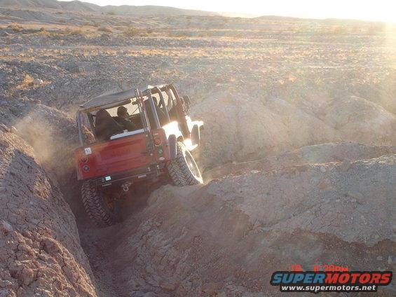 Red off-road vehicle climbing a steep dirt incline in a desert canyon