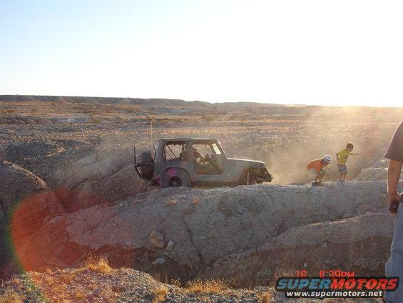 Jeep Wrangler struggling on a dirt mound with two children nearby