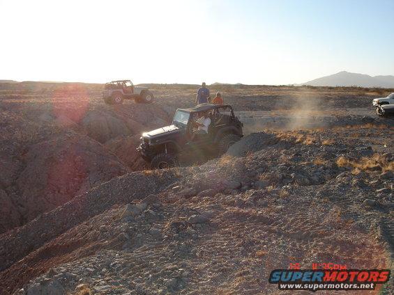 Two Jeeps off-roading in a dusty, rocky terrain with mountains in the background