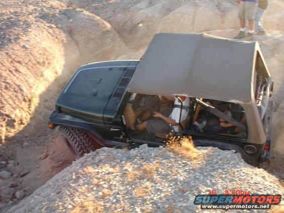 Green Jeep Wrangler off-roading on a rocky incline, soft top up, driver visible