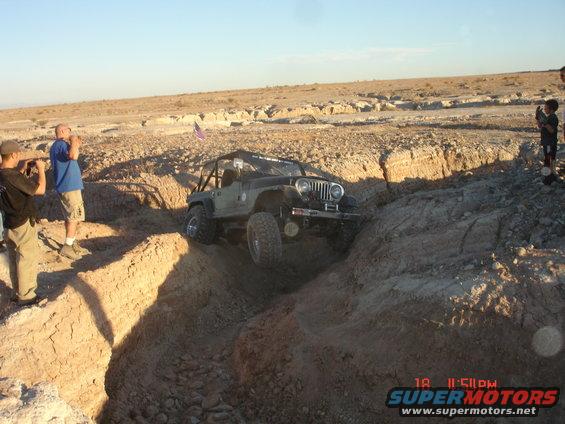 Jeep Wrangler navigating a deep rut in a desert landscape with people watching