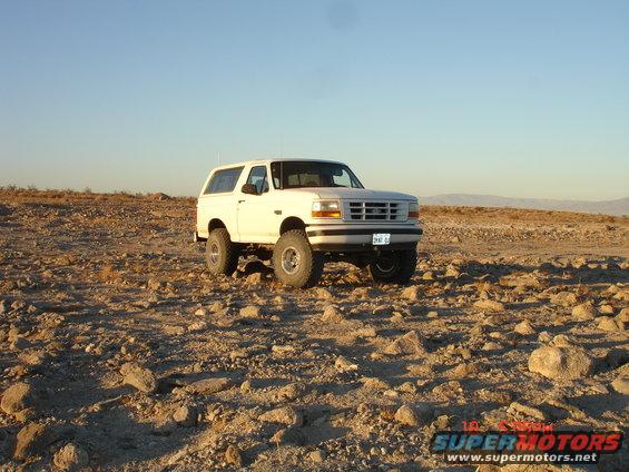 White Ford Bronco parked on rocky terrain under a clear blue sky