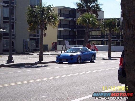 Blue 1995 Ford Probe parked on street with palm trees and motel in background