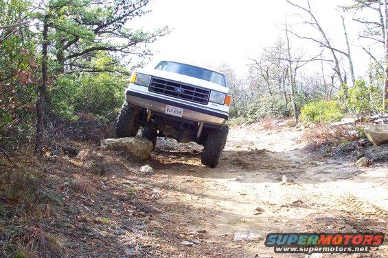 White 1987 Ford Bronco on rocky trail, front wheels on rocks