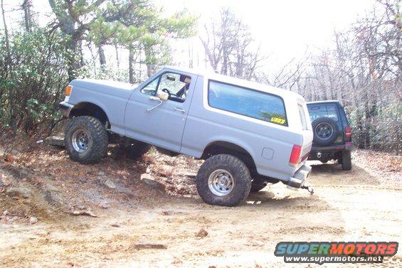 1987 Ford Bronco climbing over rocks on a dirt trail, another SUV behind it