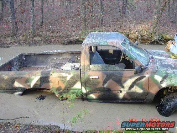 Side view of a camouflaged pickup truck stuck in mud, windshield cracked
