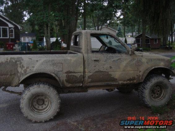 Mud-covered pickup truck, side view, showing its tires and body covered in dirt