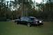 1999 Lincoln Town Car - A black sedan sits on a grassy lawn near a body of water and trees.