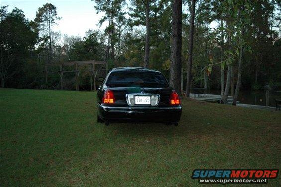 Black Lincoln Town Car parked on grass, rear view. License plate reads 11A 725