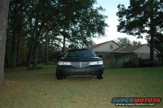 Black sedan with a chrome grille, parked on grass in front of houses