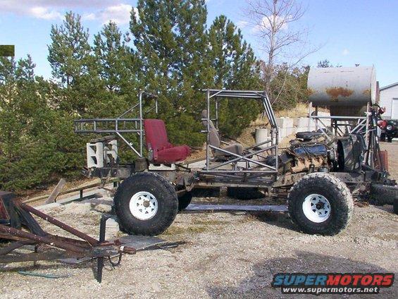 Custom off-road vehicle frame with red driver's seat, exposed engine, and large tires, parked outdoors