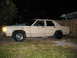 1985 Ford Crown Victoria LTD - A tan sedan sits on a grassy lawn at night, showing its side profile with modified wheels and exhaust pipes.