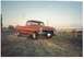 1979 Ford F-150 - A red pickup truck is parked on a dirt road with a wooden fence behind it under a clear sky.