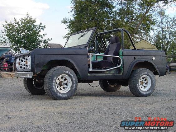 Black 1968 Ford Bronco with no doors and a roll cage, parked on gravel