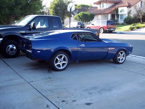 Blue 1971 Ford Mustang side view, parked next to a black pickup truck
