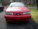 1995 Ford Taurus - A red 1995 Ford Taurus is parked in front of a house, with another dark car visible to the left.