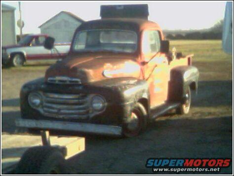 Rusty orange pickup truck, front end visible, with another truck in background