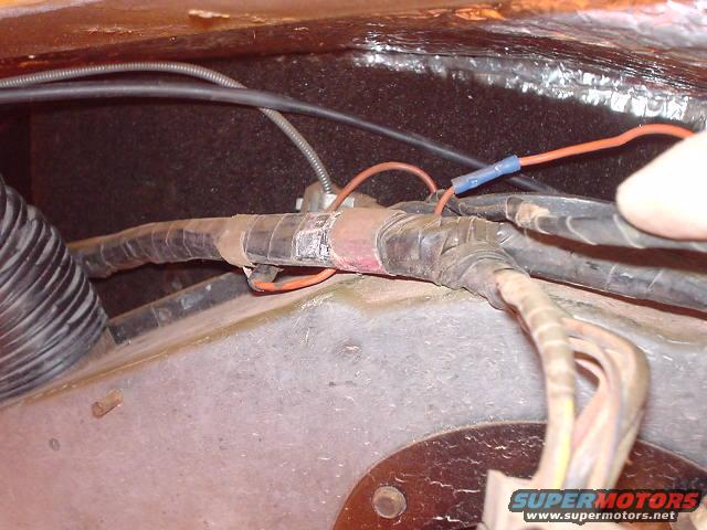 Close-up of a vehicle's wiring harness with electrical tape and conduit. A blue connector is visible
