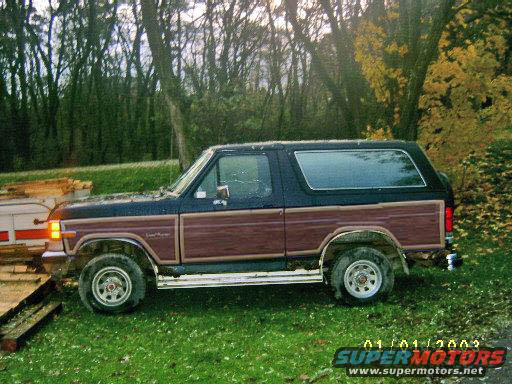 Dark blue and wood-paneled Ford Bronco parked on grass, side view