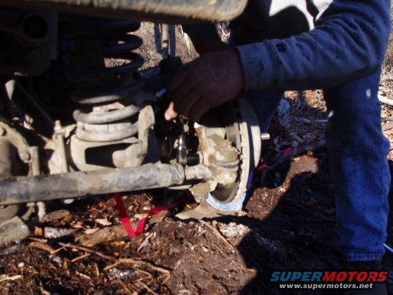 Close-up of a vehicle's front suspension and brake assembly with a person working on it