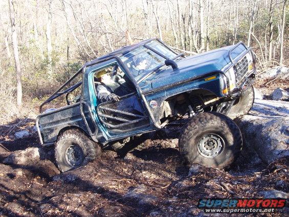 Green off-road pickup truck with roll cage navigating rocks and mud