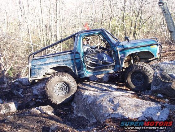Teal off-road truck with roll cage and large tires climbing over rocks