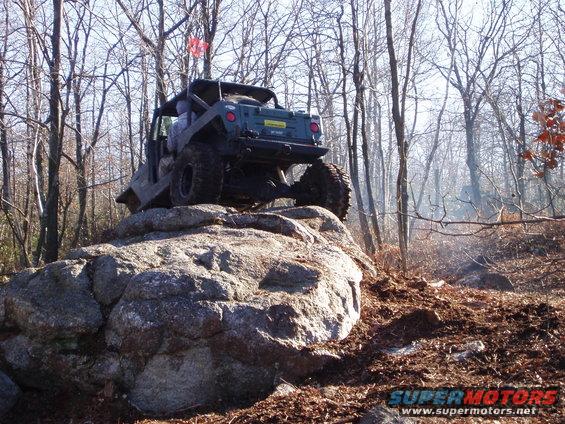 Off-road vehicle with large tires climbing over a boulder in a wooded area