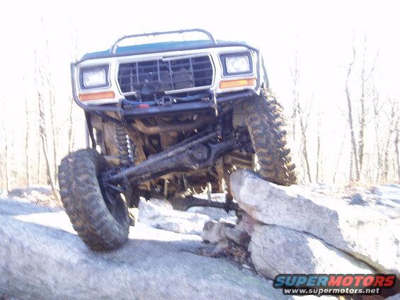 Green off-road truck with large tires climbing over rocks, front view