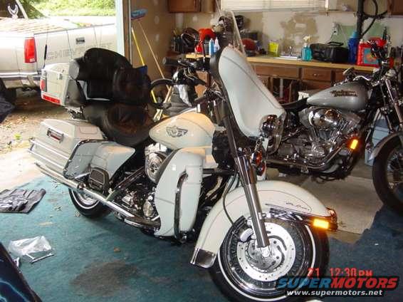 Two motorcycles parked in a garage, one white and one silver, with a white pickup truck visible in the background