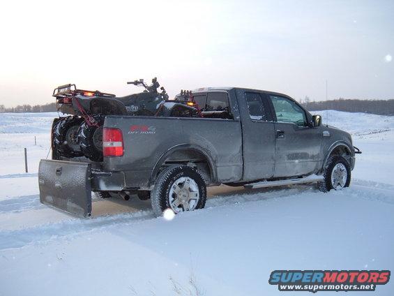 Gray Ford F-150 pickup truck with a plow and an ATV in the bed, stuck in snow