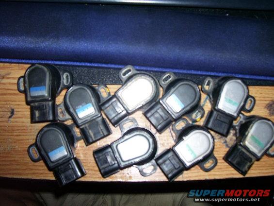 Several throttle position sensors laid out on a wooden surface. Some have blue labels, others have white or green labels